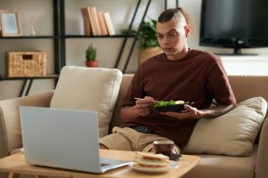 A guy is enjoying with his meal and watching OTT content on a laptop