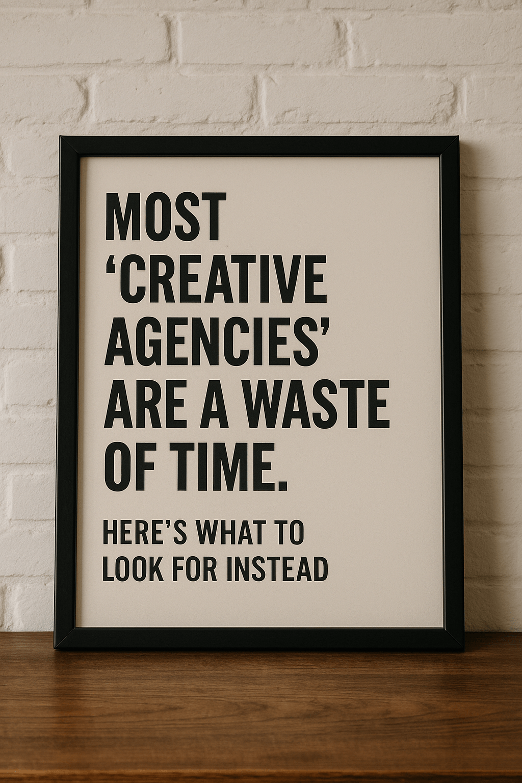 Framed sign with bold black text reading "Most Creative Agencies Are a Waste of Time. Here's What to Look for Instead" against a white brick wall.