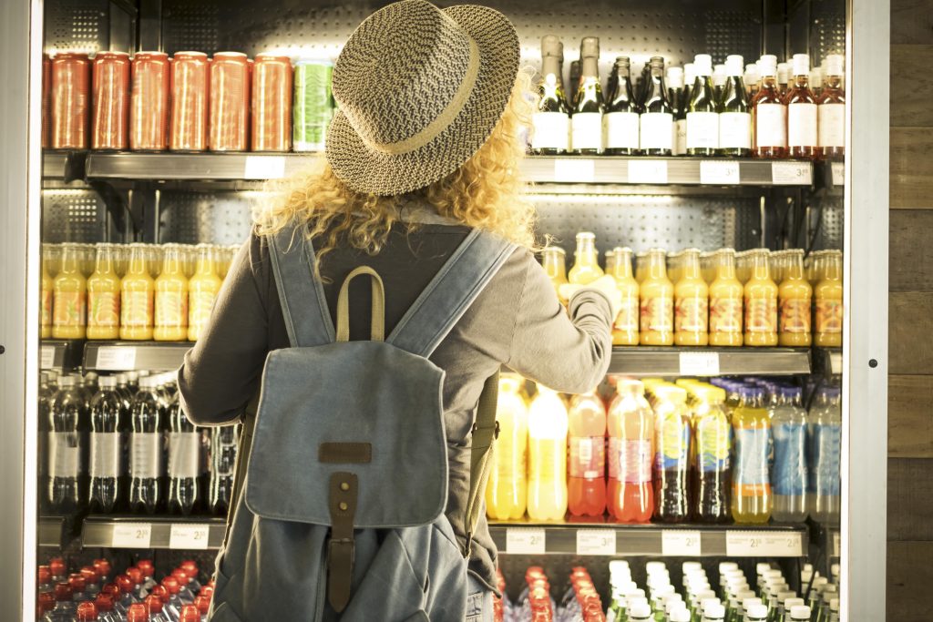 Woman selecting bottled drinks from a store shelf, representing food and beverage CPG marketing trends for the 2025 CPG Social Media Benchmark Report.