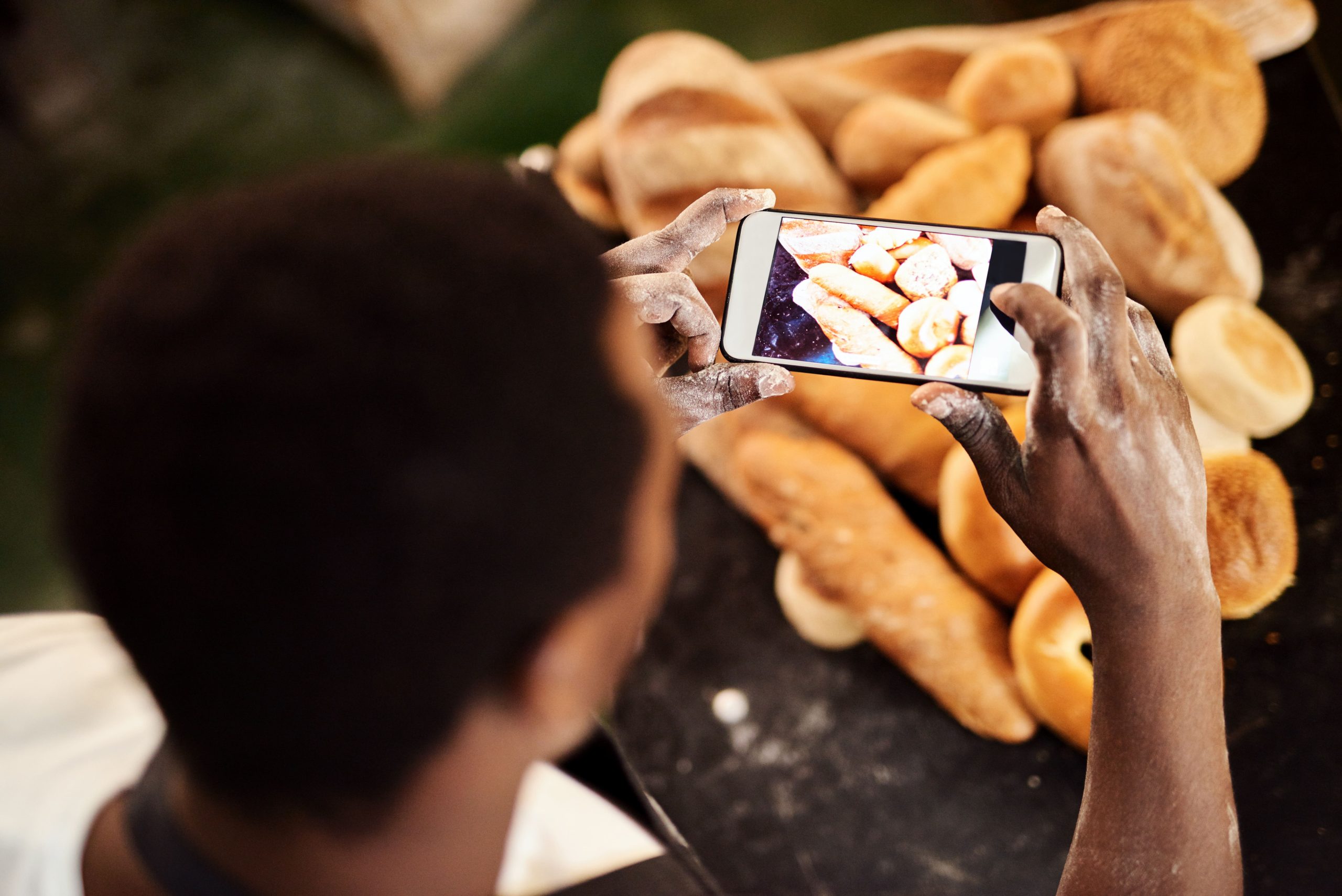 Person taking Instagram photo of fresh bread loaves for social media marketing