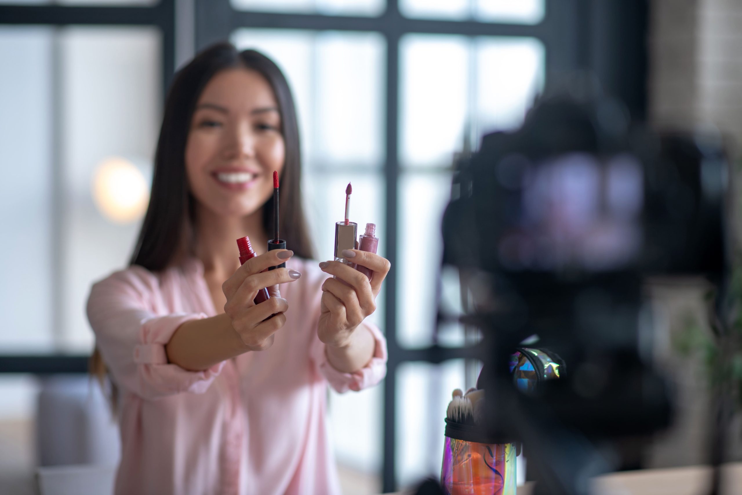 Smiling beauty influencer recording a TikTok video showcasing lipsticks for social media marketing
