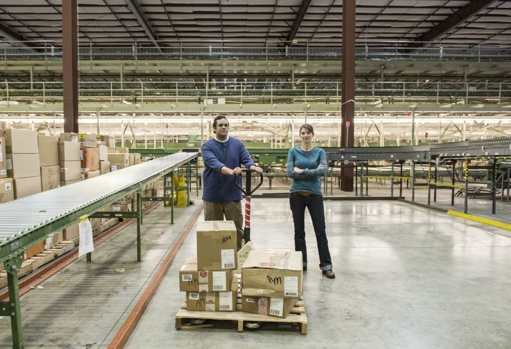 Workers in a large warehouse moving CPG boxes on a pallet for Amazon shipping.