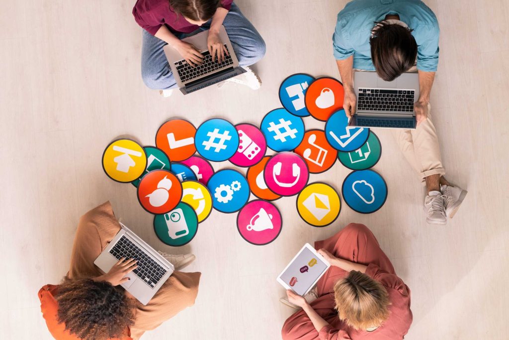 Four marketing professionals sitting with laptops surrounded by colorful paid social media icons, planning a paid social ad strategy